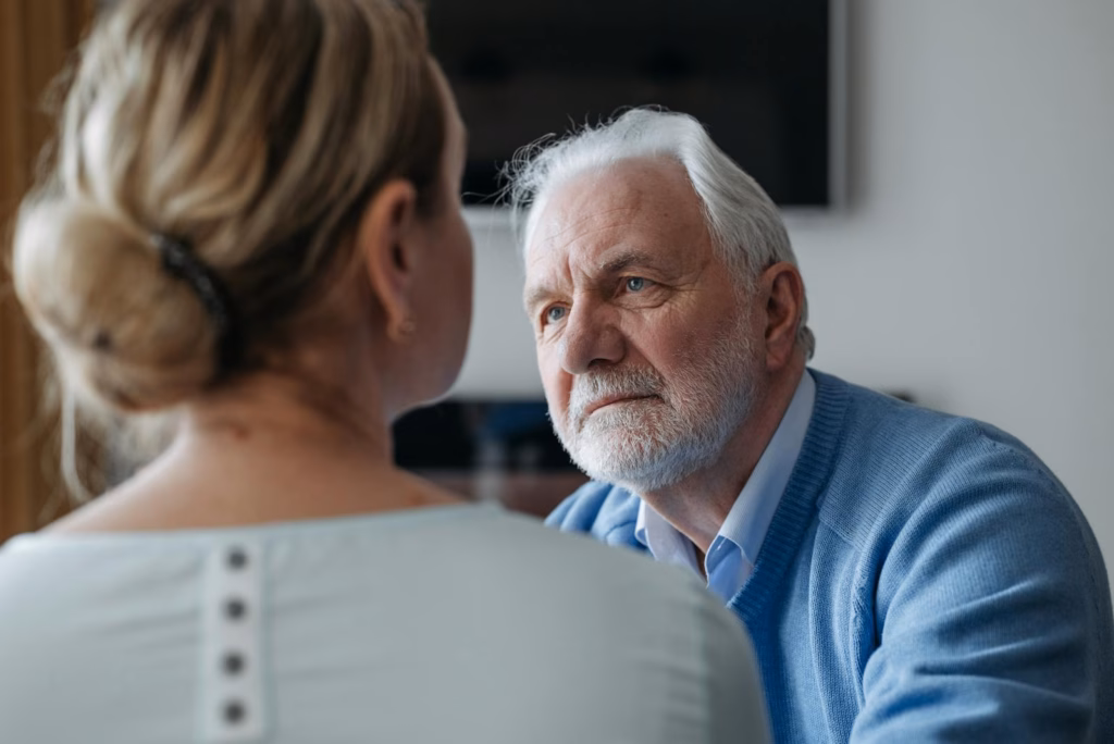 A thoughtful elderly man with grey hair having a conversation indoors, focused on a woman.